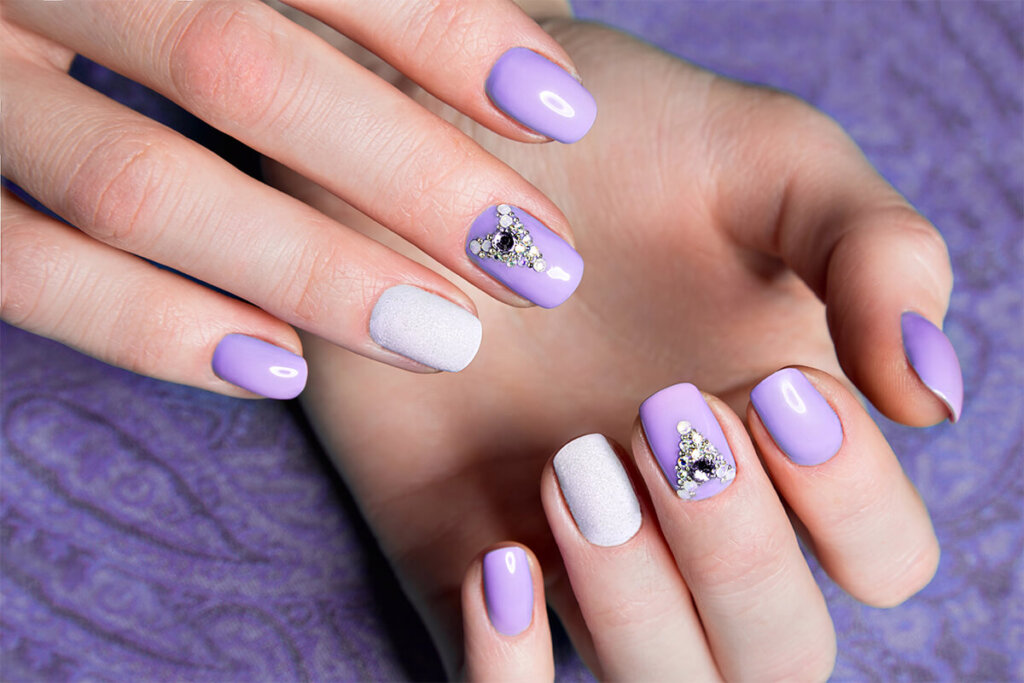 Beautiful purple manicure with crystals on female hand. Close up