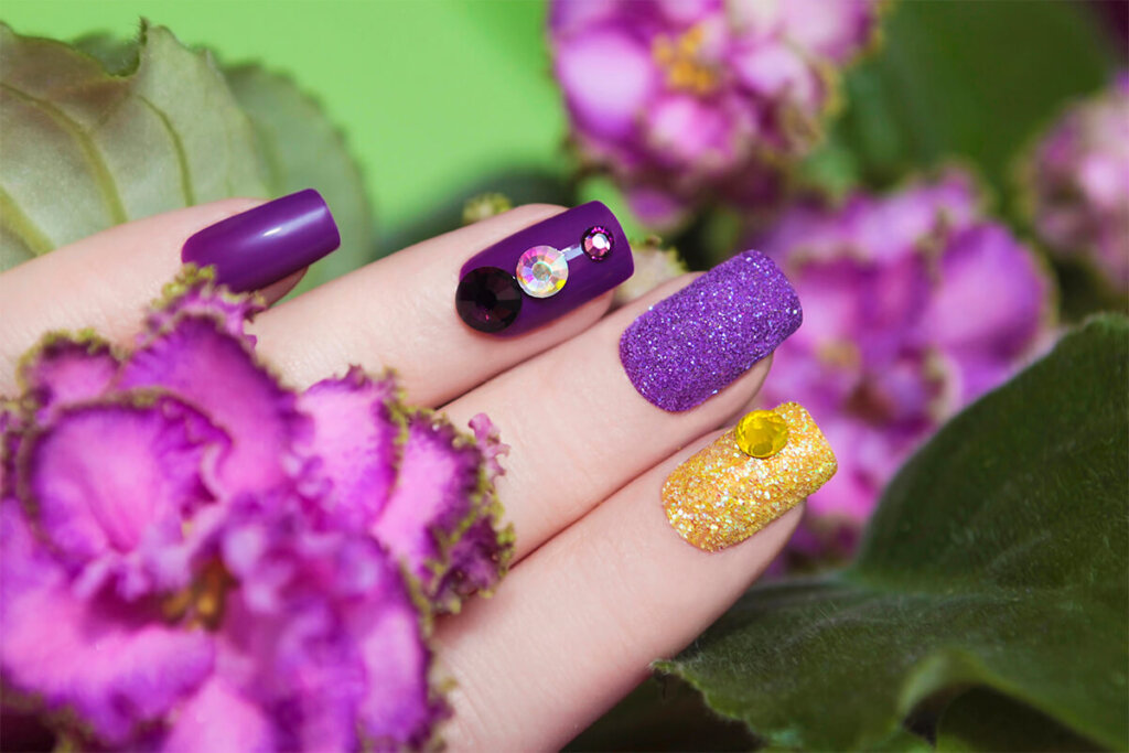 a hand with purple and yellow nails with rhinestones